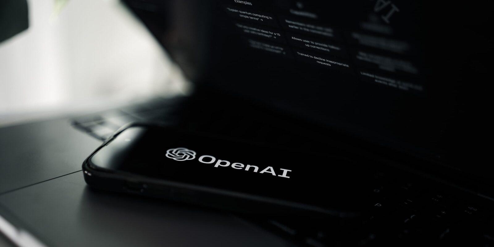 Illustration OpenAI. Smartphone mit OpenAI Logo auf einem MacBook