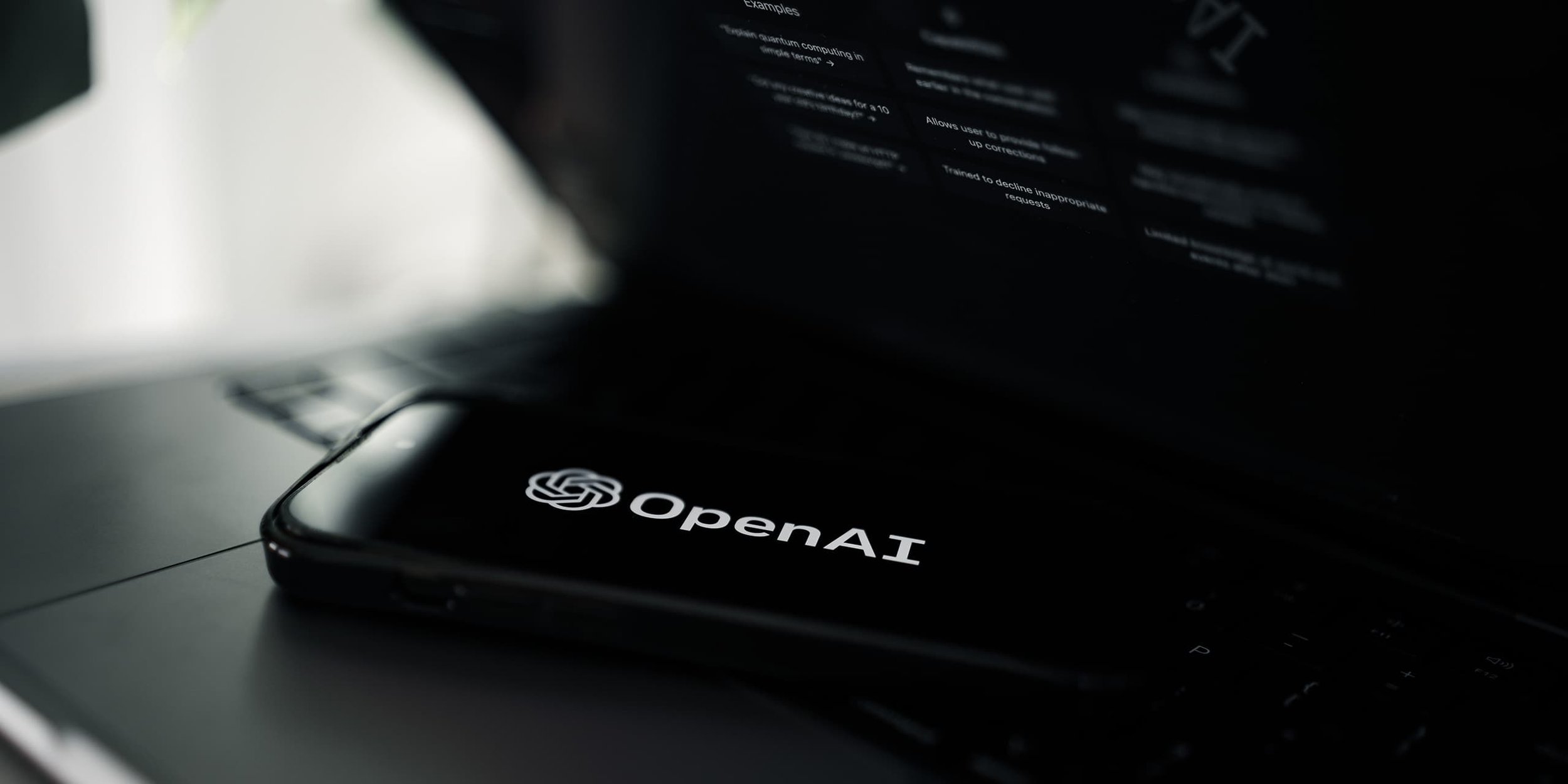 Illustration OpenAI. Smartphone mit OpenAI  Logo auf einem MacBook